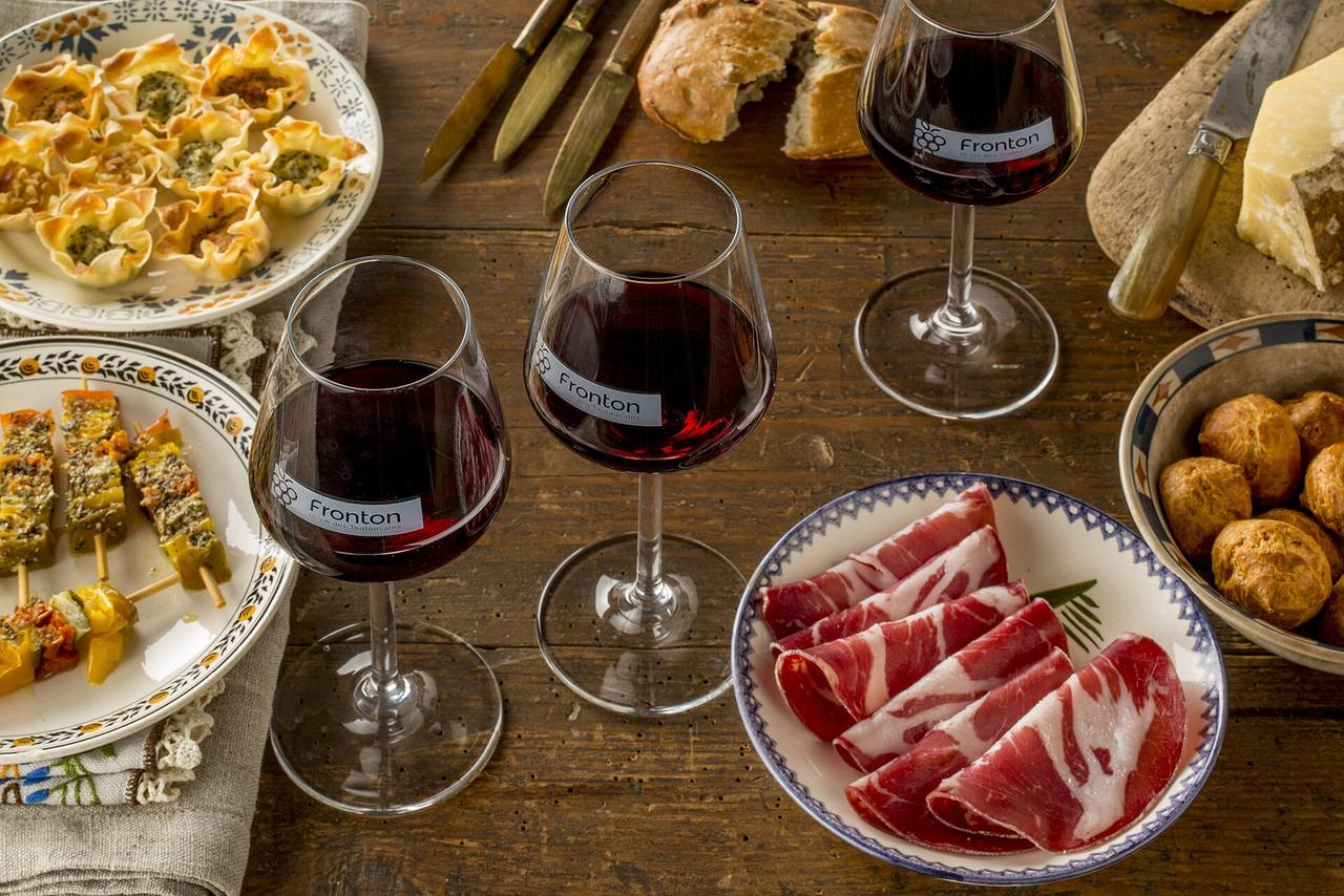 Table de dégustation avec verres de vin Fronton, charcuterie, tapas et pain sur table en bois.
